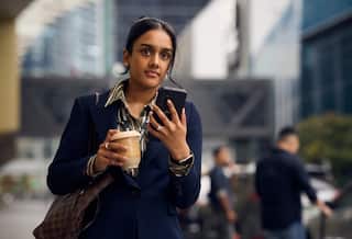 A woman wearing a suit walking in the street and holding a phone.