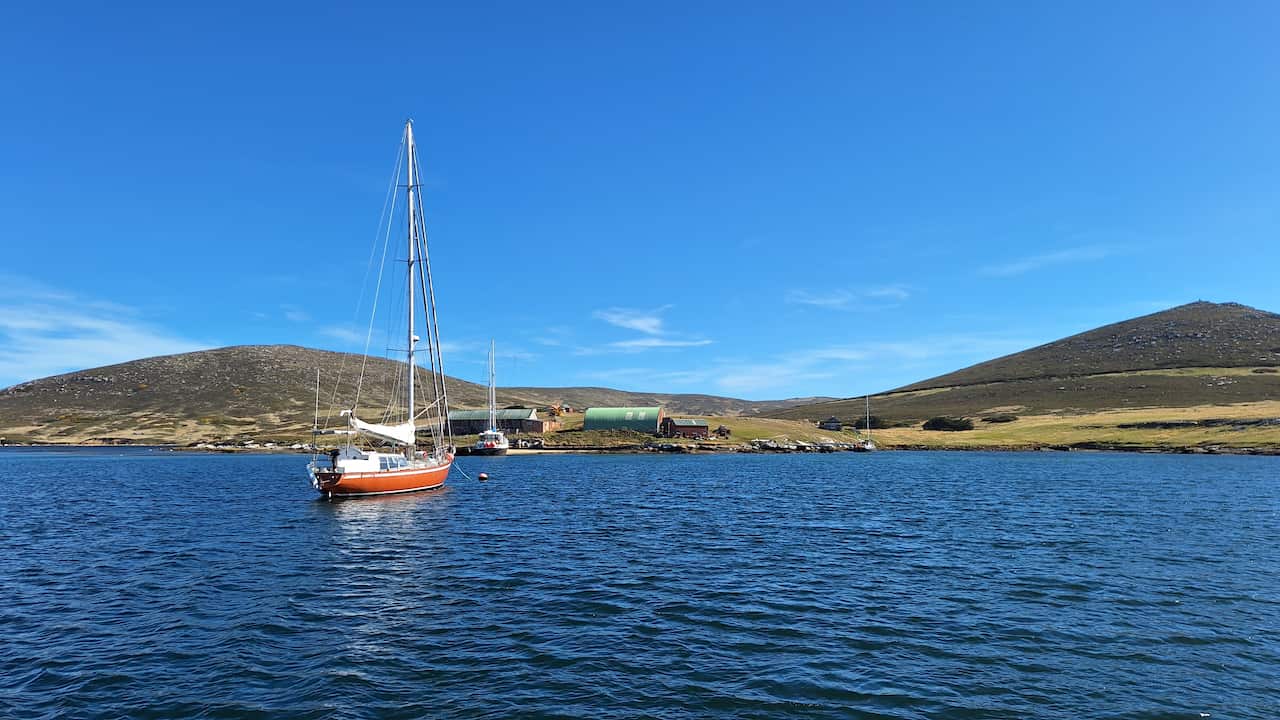 A boat in a dark blue harbour against a hilly, barren backdrop and blue sky.