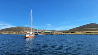 A boat in a dark blue harbour against a hilly, barren backdrop and blue sky.