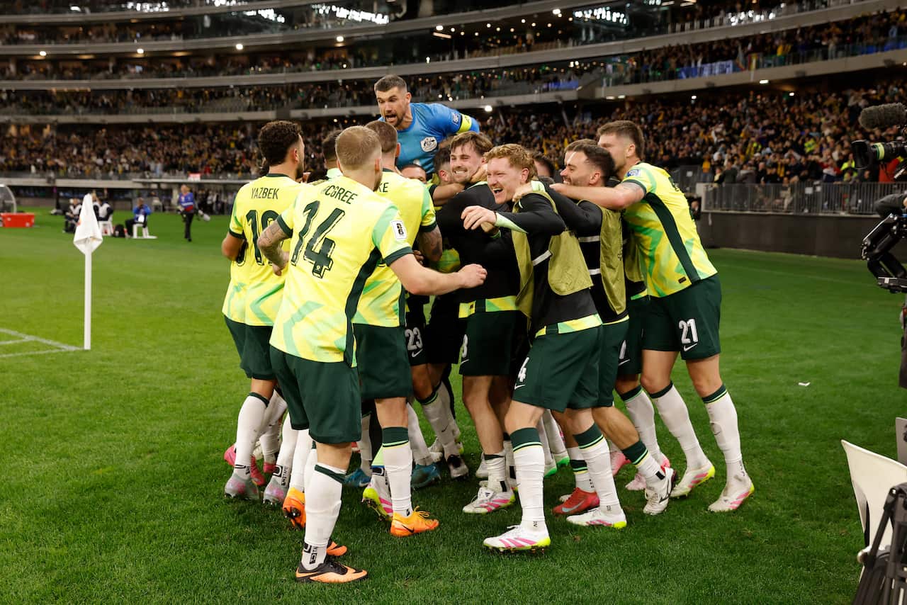 A group of footballers in yellow and green strip embrace in a huddle of celebration on the side of the field 