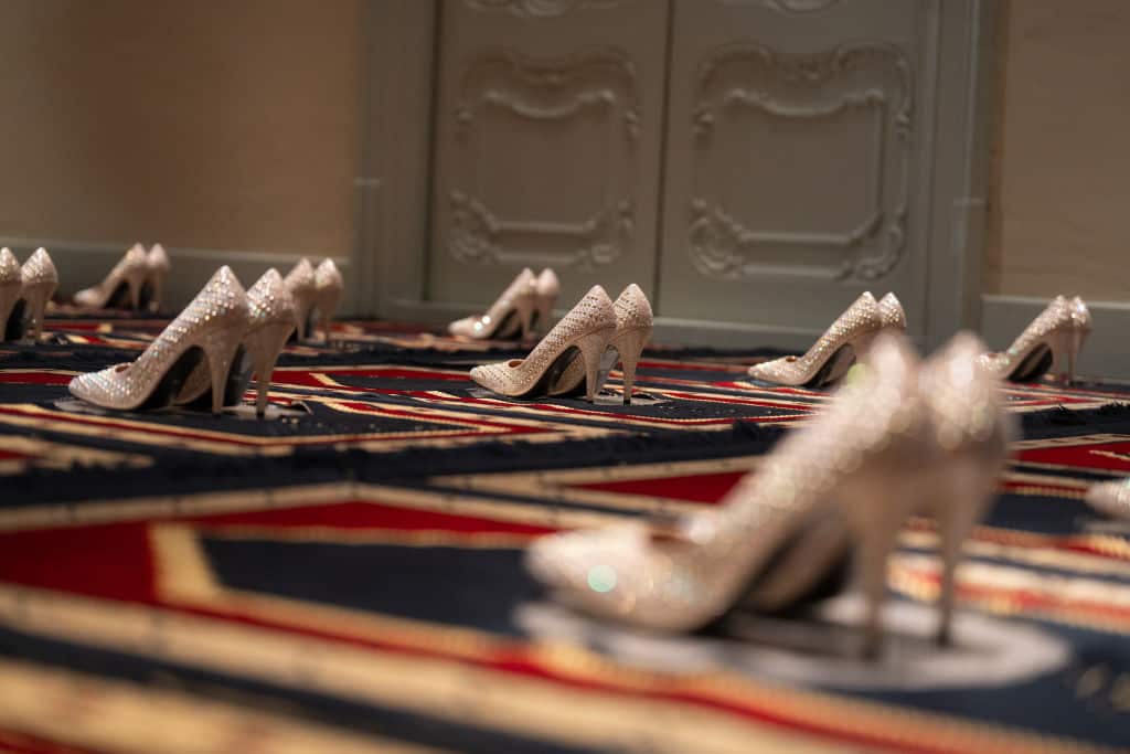 A collection of stilettos are placed on prayer mats for a piece of art.