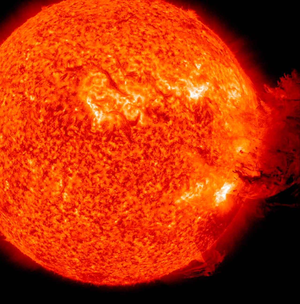 A bright and red and orange sun with a textured surface sits slightly off centre as an explosion of darker red comes from the right of the sun into dark space