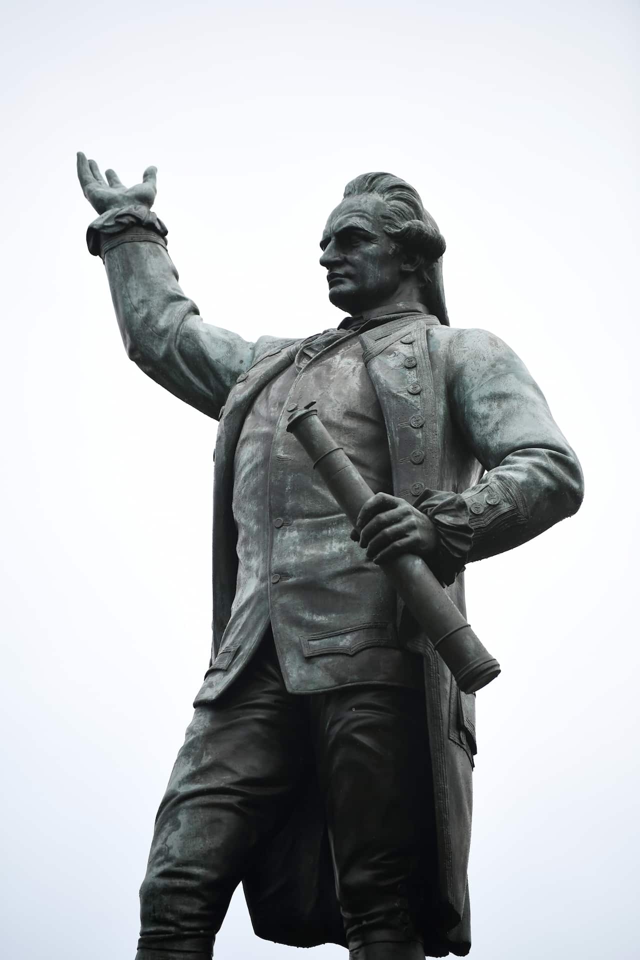 A statue of a captain, he stands with a tele scope in one hand and the other raised in the air