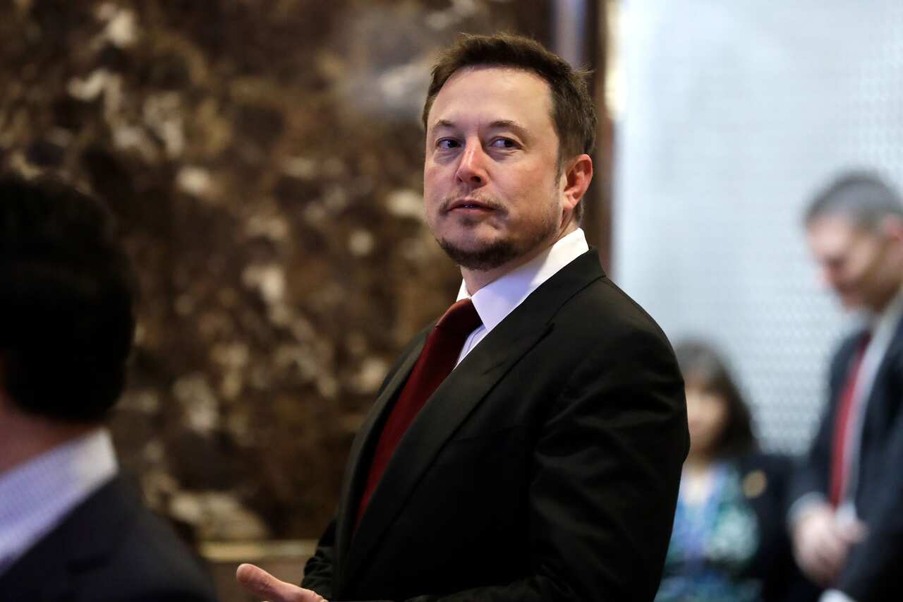A side profile of a man wearing a black suit and a red tie.