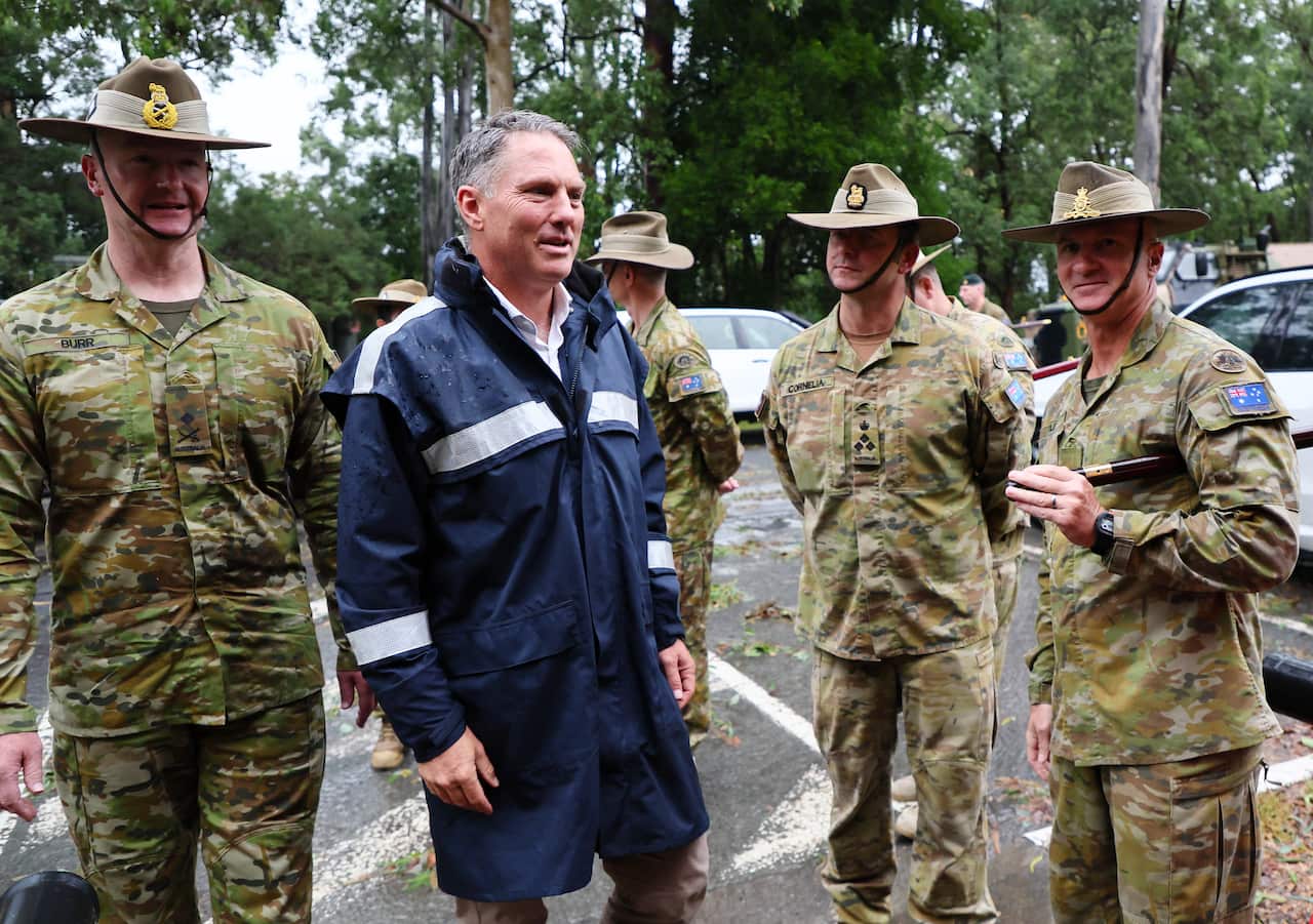 A man in a navy rain jacket, standing next to ADF personnel.