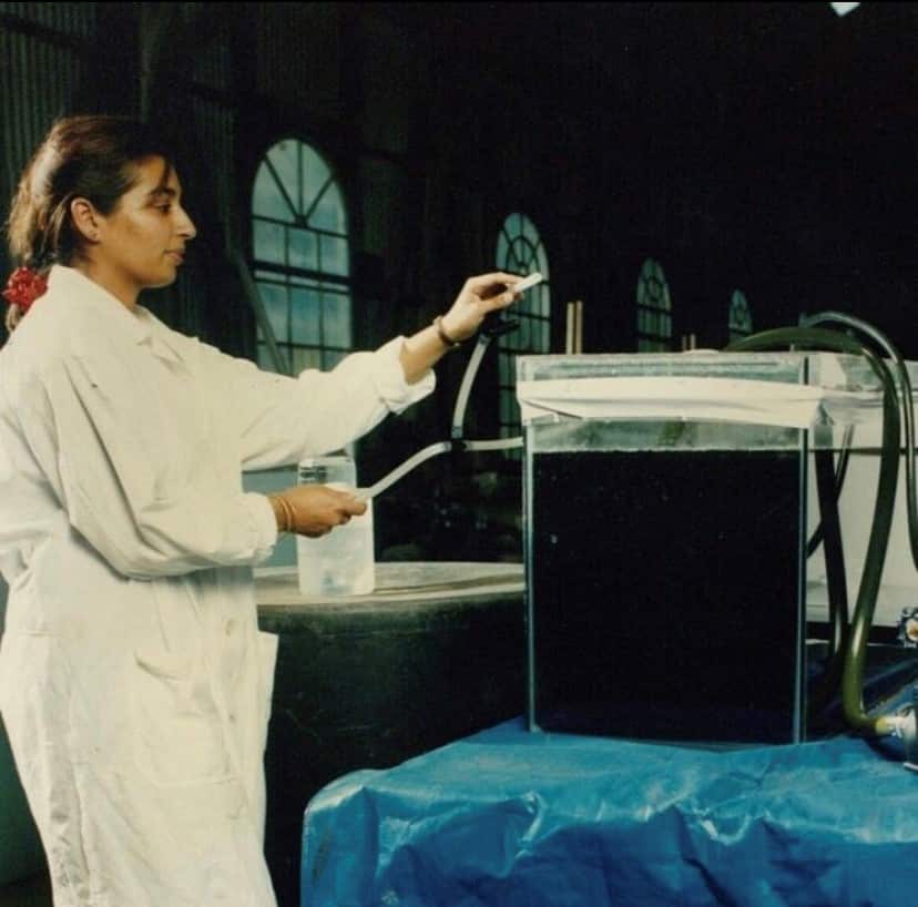 Mehreen Faruqi wearing a white coat and standing next to a clear tank containing liquid. 