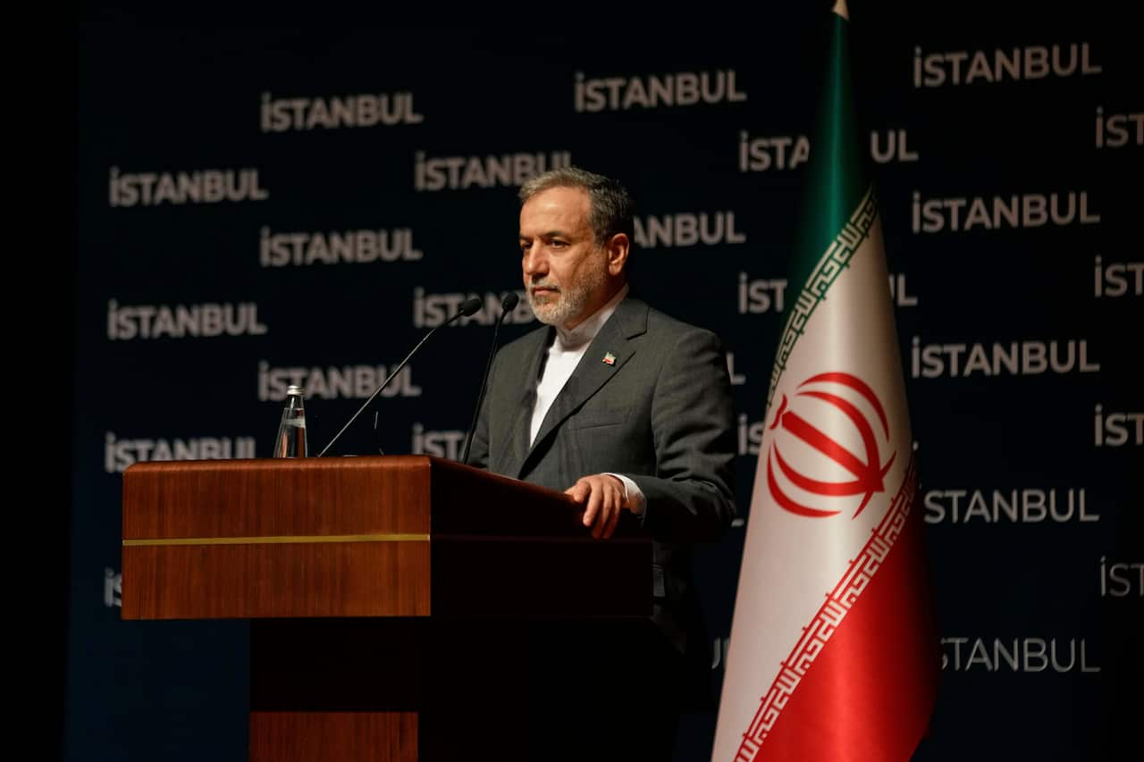 Iranian Foreign Minister Abbas Araghchi stands at a lectern wearing a suit. 