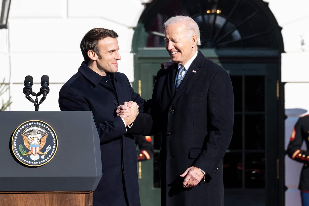Two men wearing suits stand near a lectern and shake hands. 