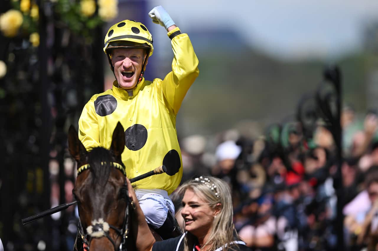 A man in a yellow jersey with black dots raises his fist in celebration while riding a horse
