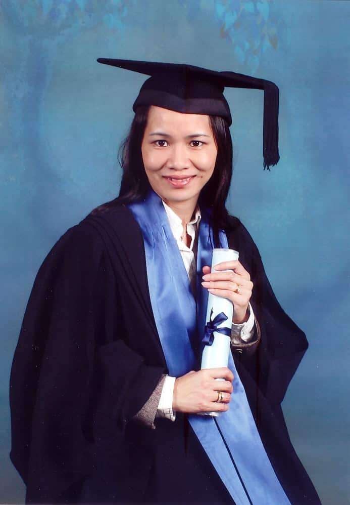 A woman in graduation robes holding a diploma and smiling at camera.