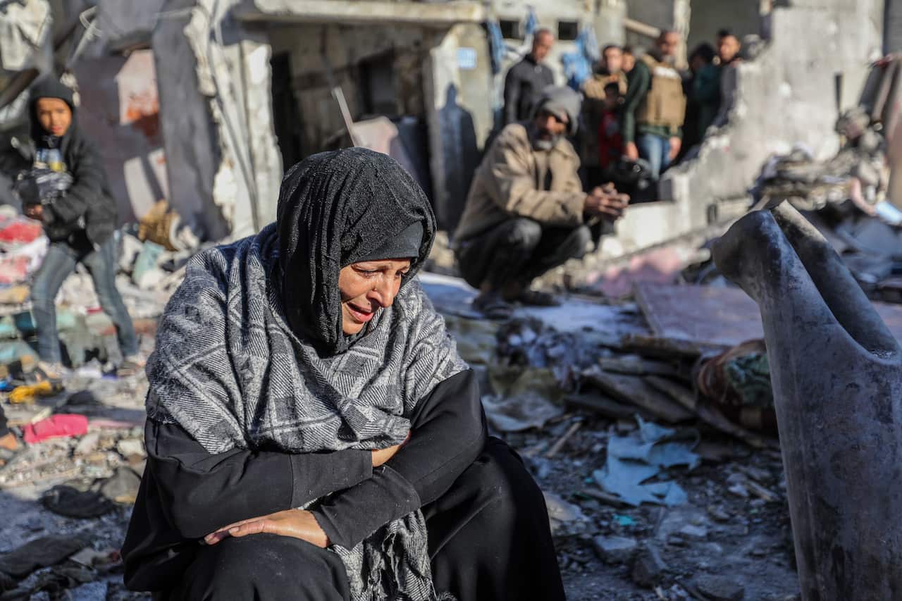 A woman looking distraught among the rubble of destroyed buildings.