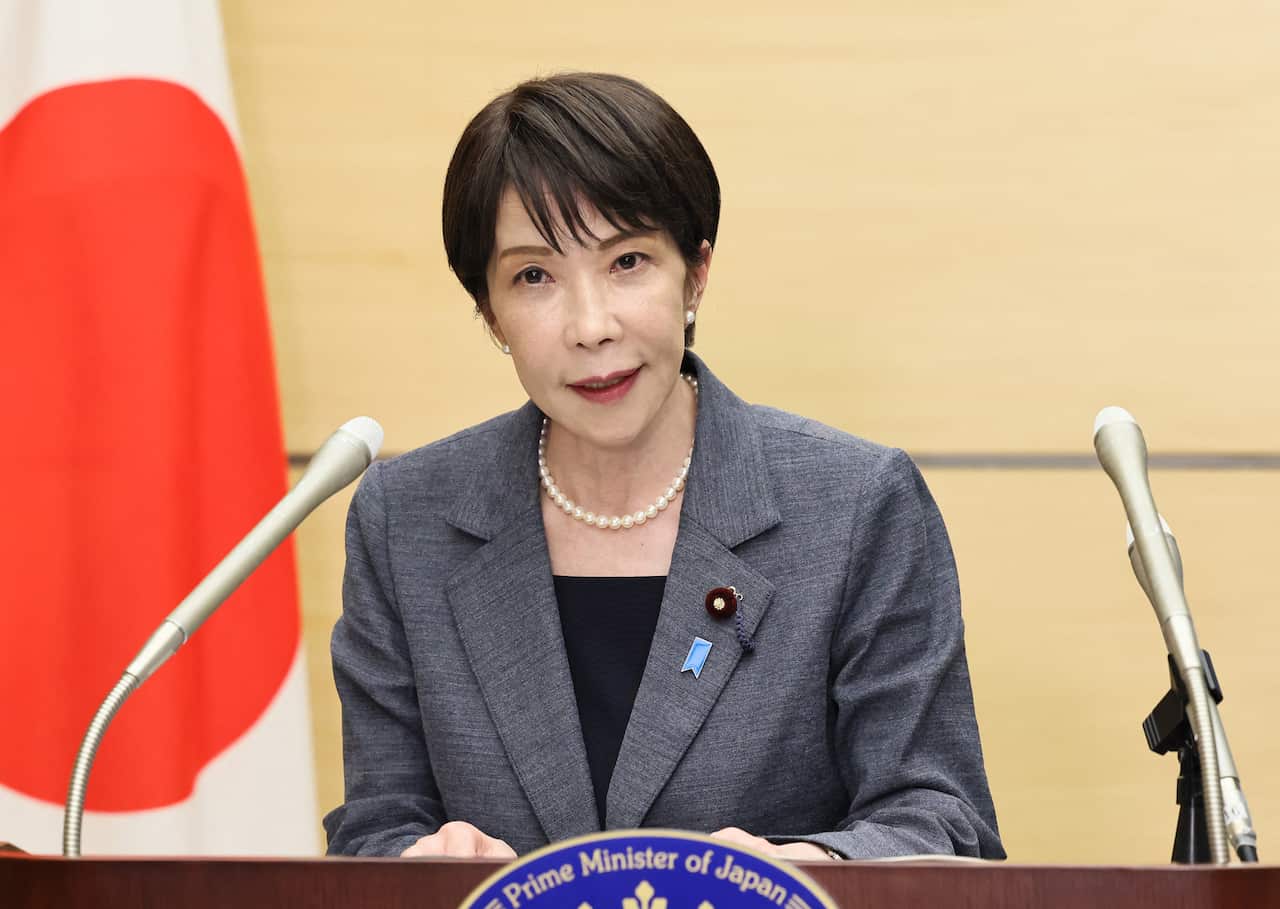 Japan's PM Sanae Takaichi in a grey suit speaks at a lectern.