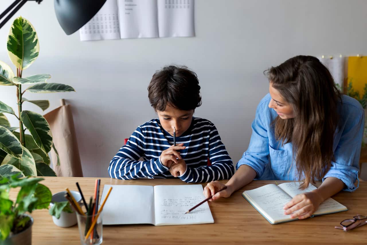 Female tutor explaining to boy through book on table at home