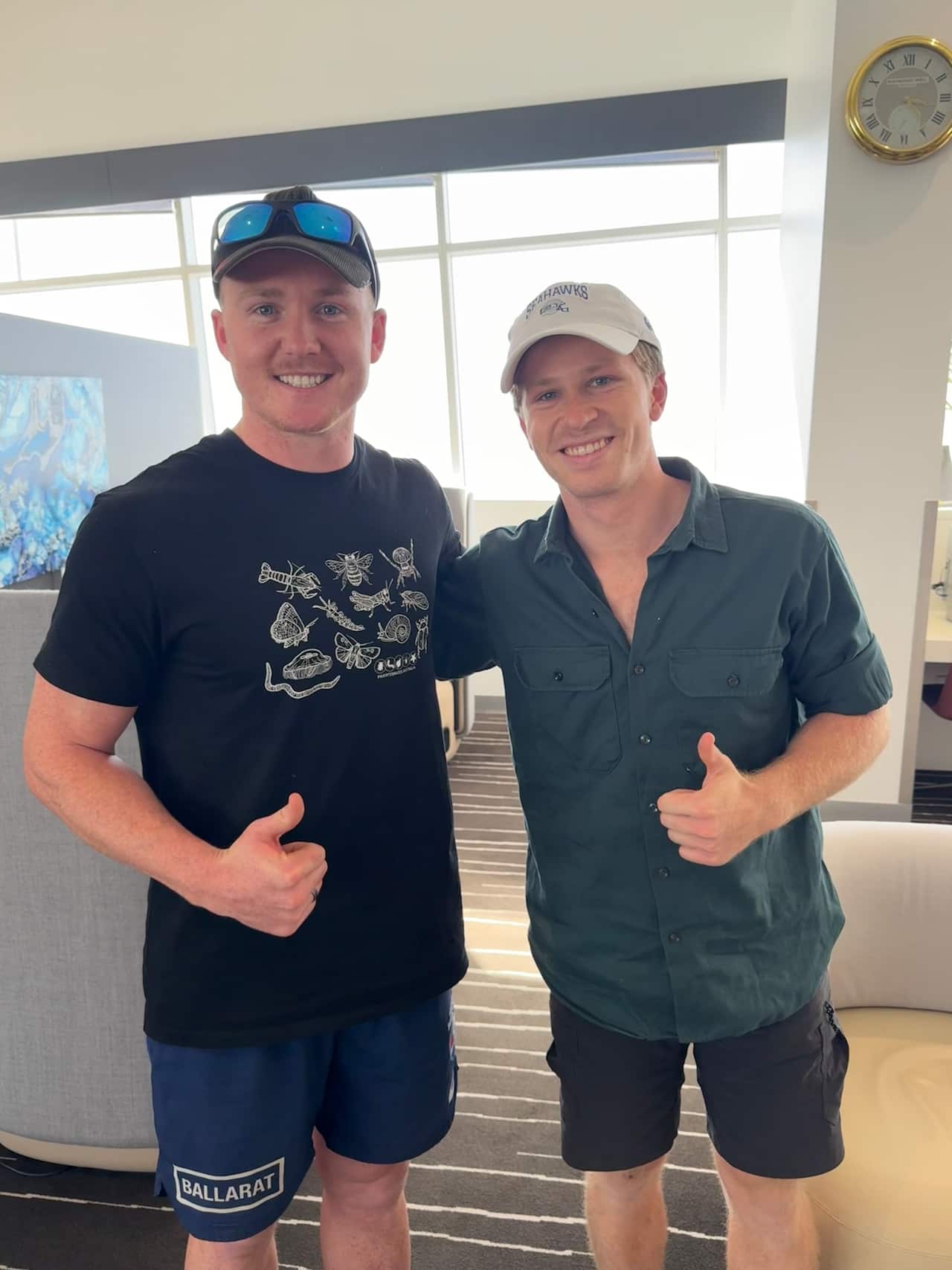 Two young white men standing beside each other, giving a thumbs up