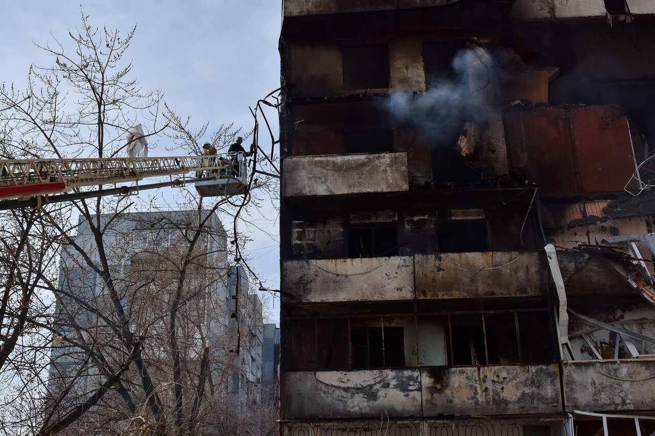 Firefighters on an aerial ladder inspecting a burnt-out building.