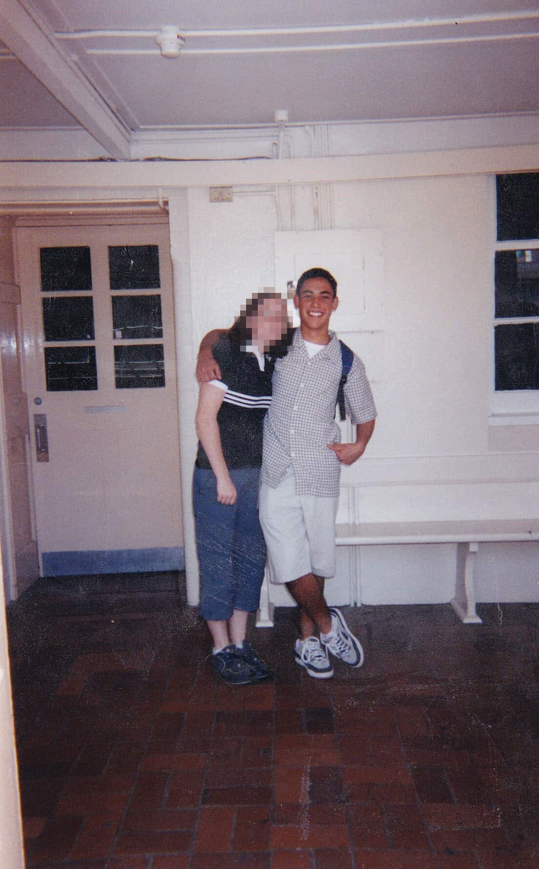 A young man in light-coloured shorts and shirt with his arm around a young woman. The pair are posing for a photo
