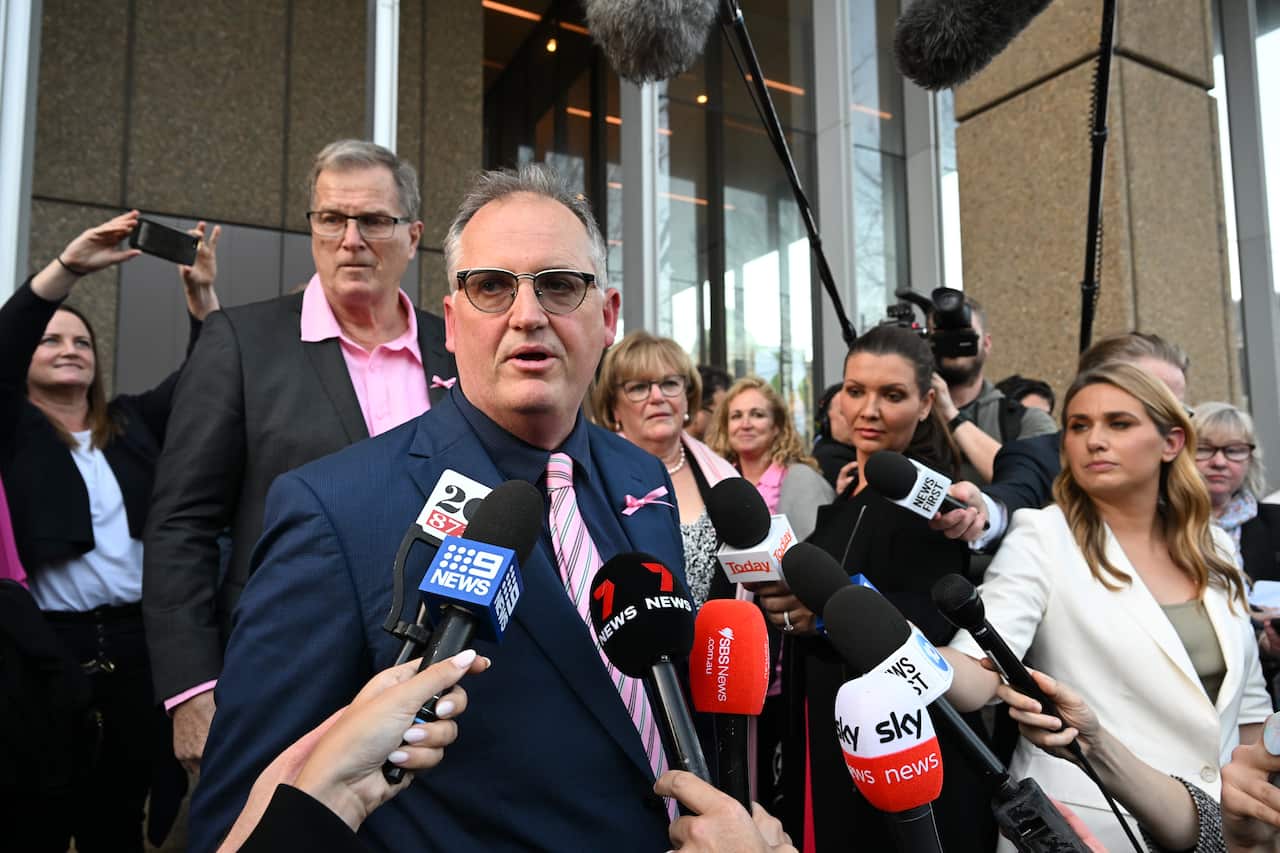 A man speaking into microphones being held by jorunalists.