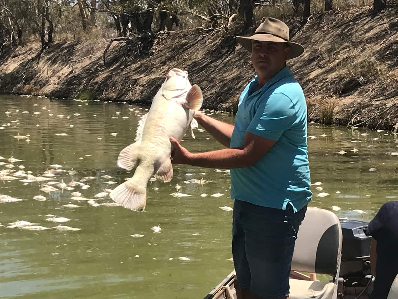 A man standing in a boat holding a dead fish