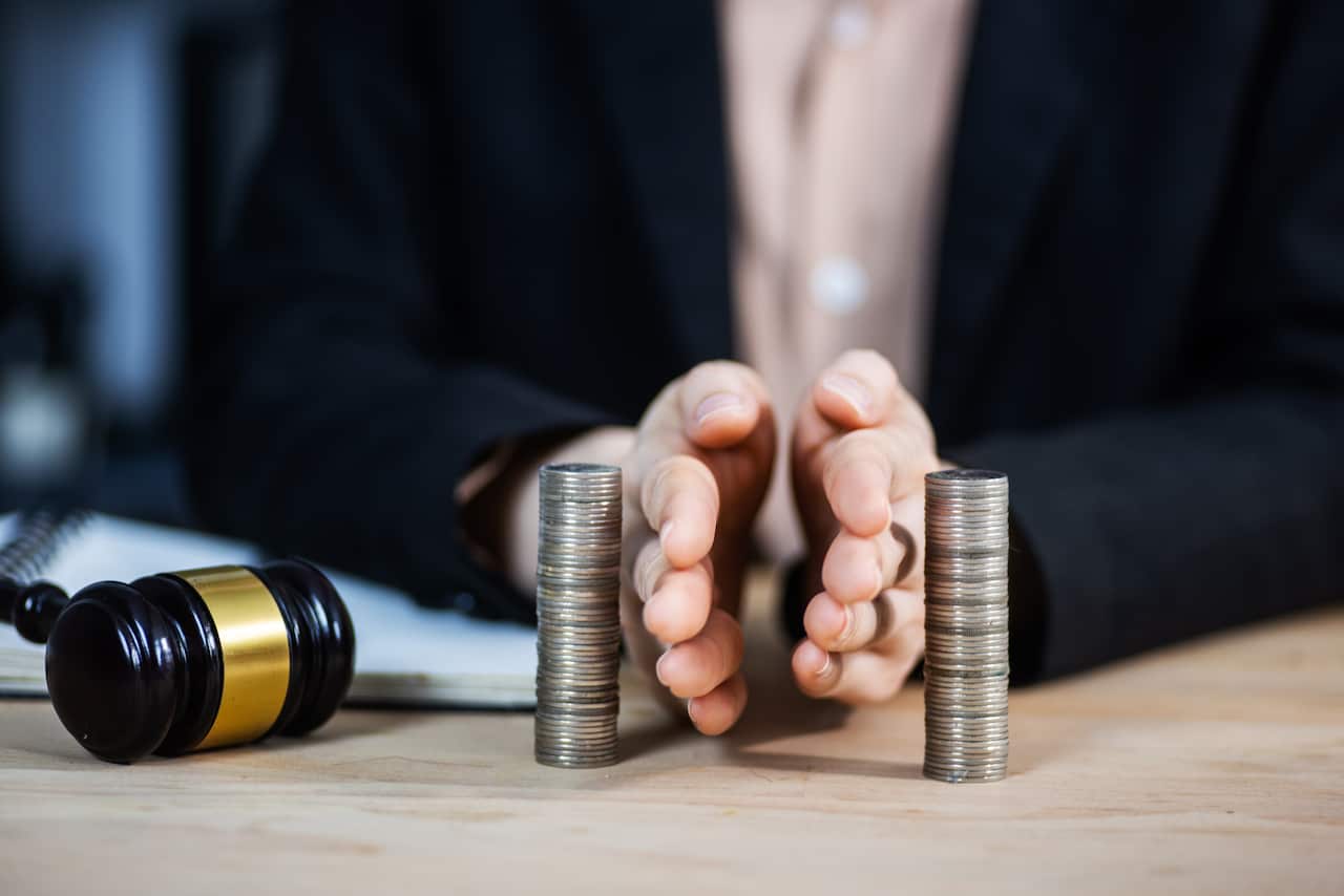 Hands separating stacks of coins placed on a wooden table next to a gavel.