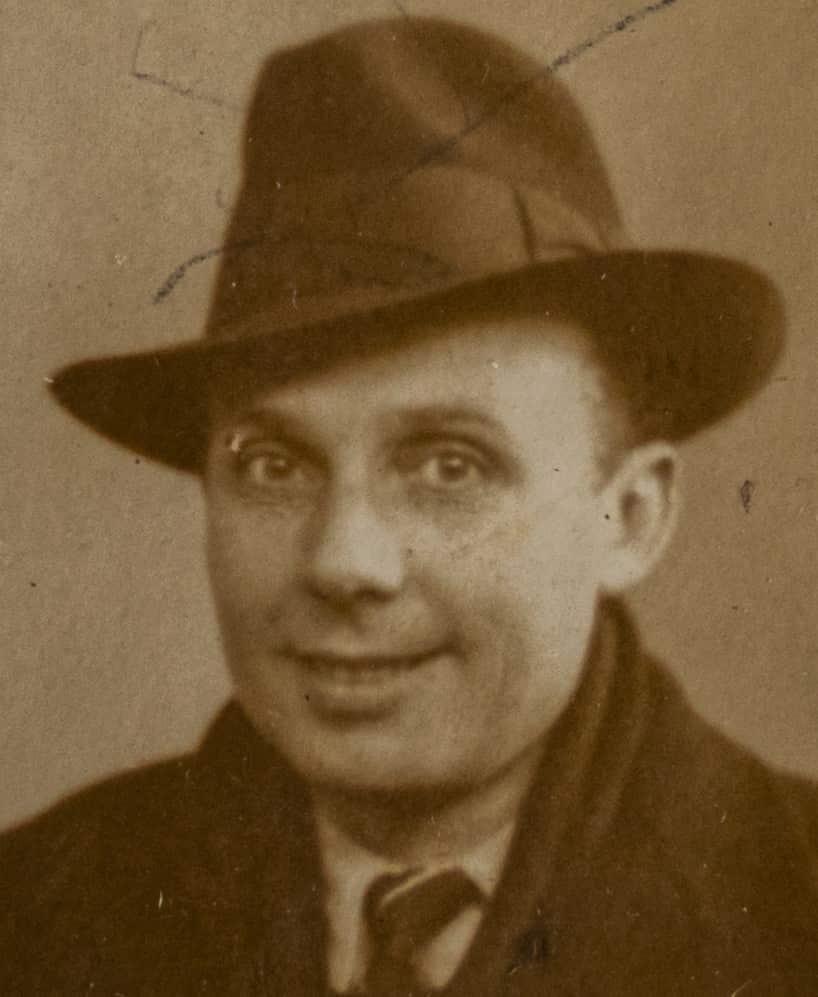 A sepia photo of man in a brown suit and hat smiling at camera.