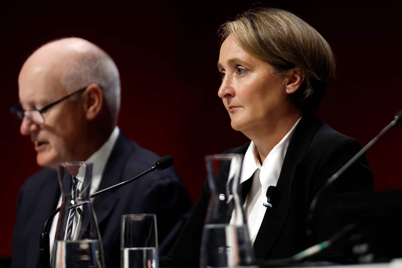 A man and woman wearing formal attire seated at a desk in front of microphones.
