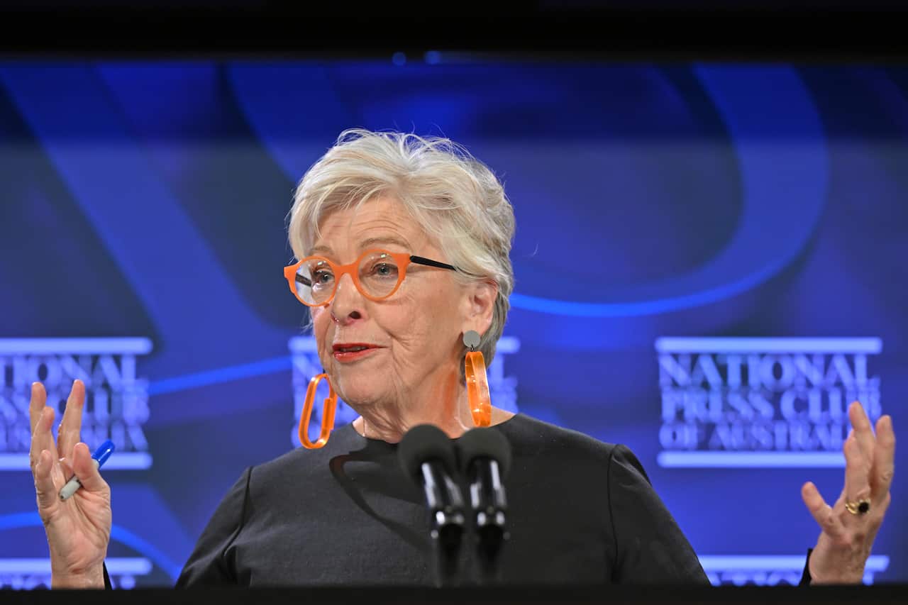 A woman in a black shirt holding her hands up wearing orange glasses and earrings