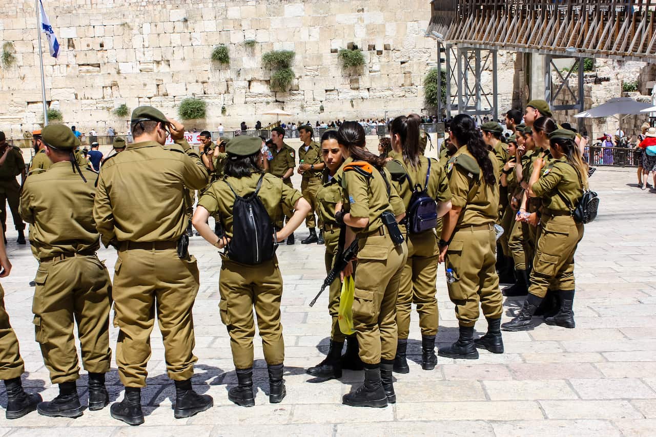 A group of soldiers wearing the khaki uniform of the IDF stand in front of the Western Wall in Jerusalem.