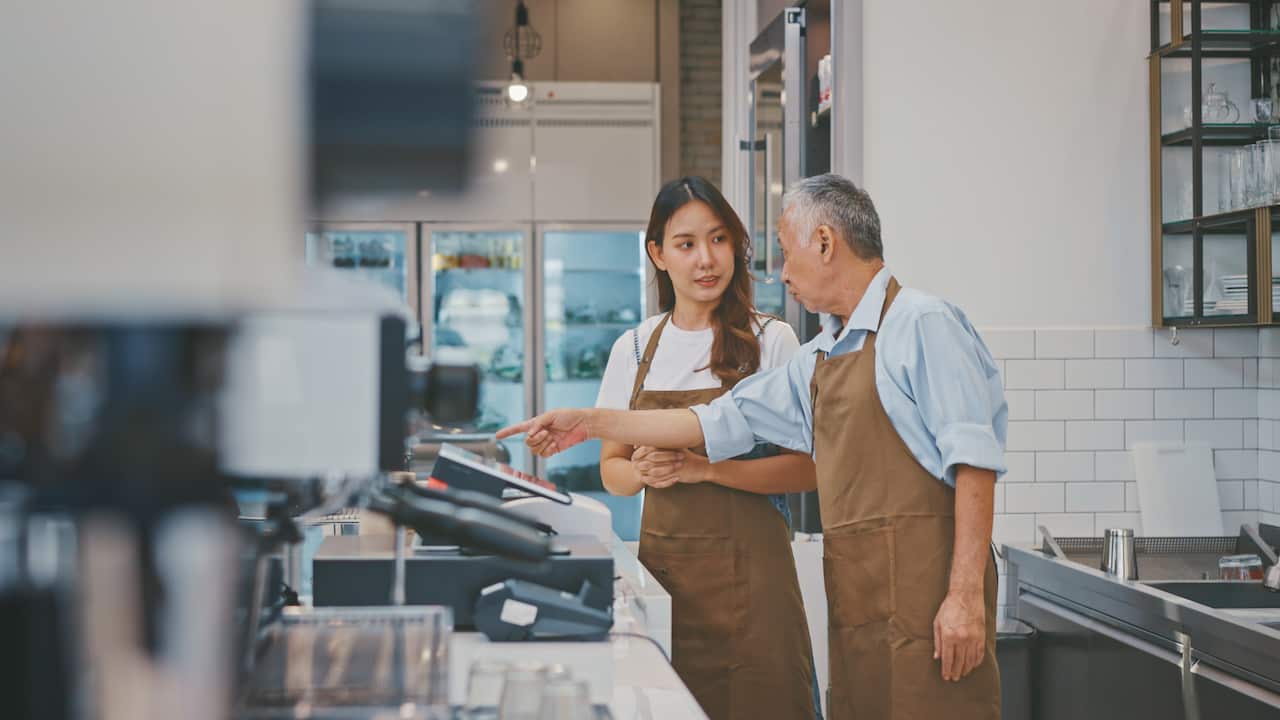 Senior Business Owner teaching a new employee in his coffee shop