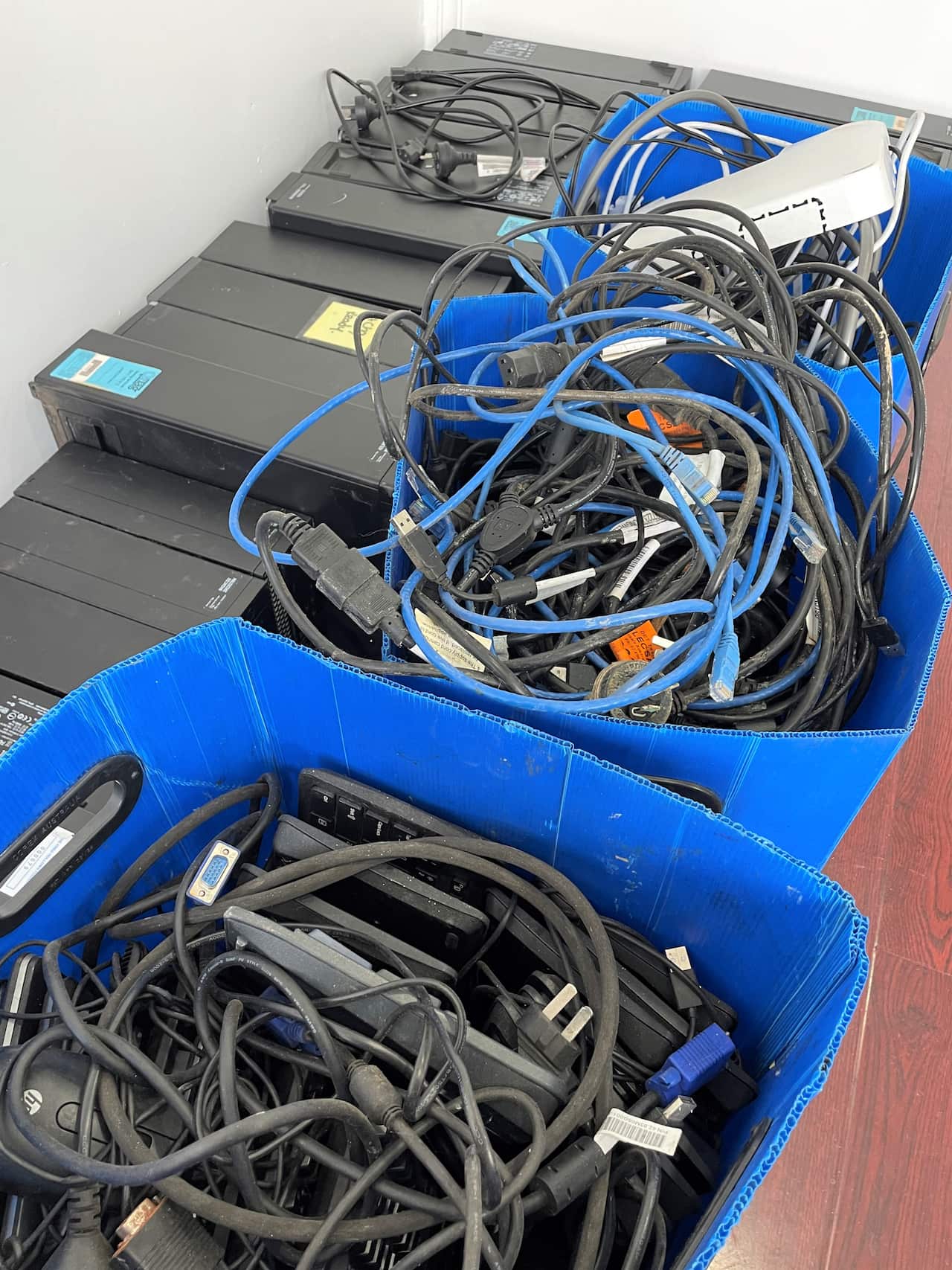 Used cables and computers stacked against a white wall.