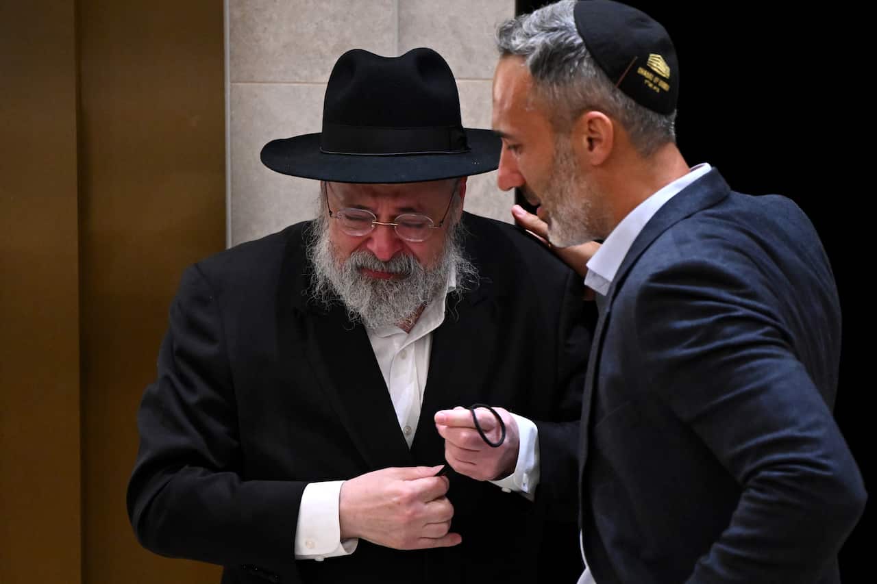 A man wearing a black hat is being consoled by a man wearing a kippah.