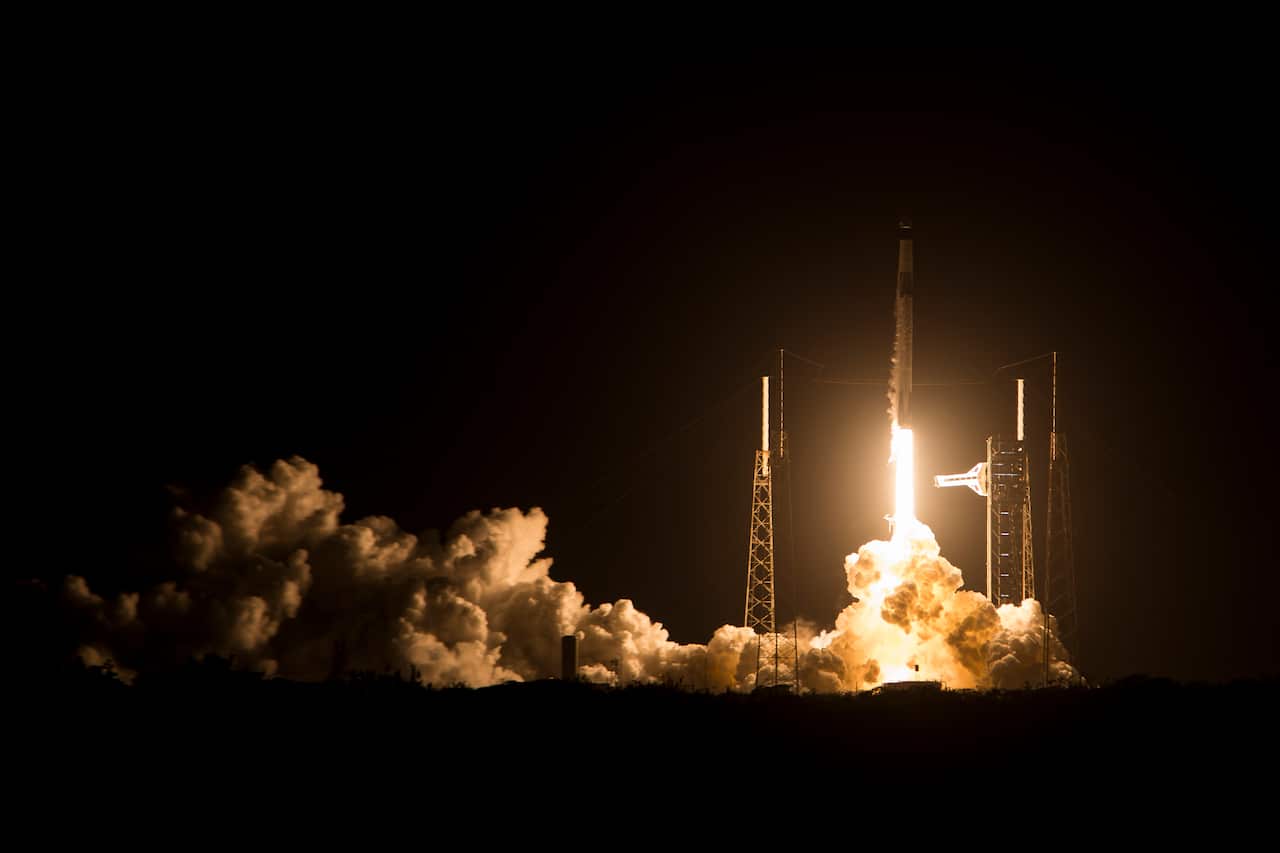 A rocket launches towards the sky with fire and a plume and smoke below.