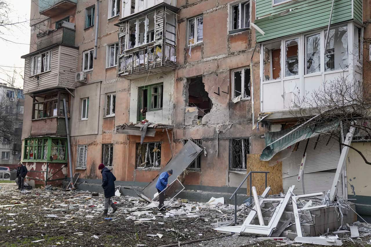 People are seen walking next to a damaged apartment building.