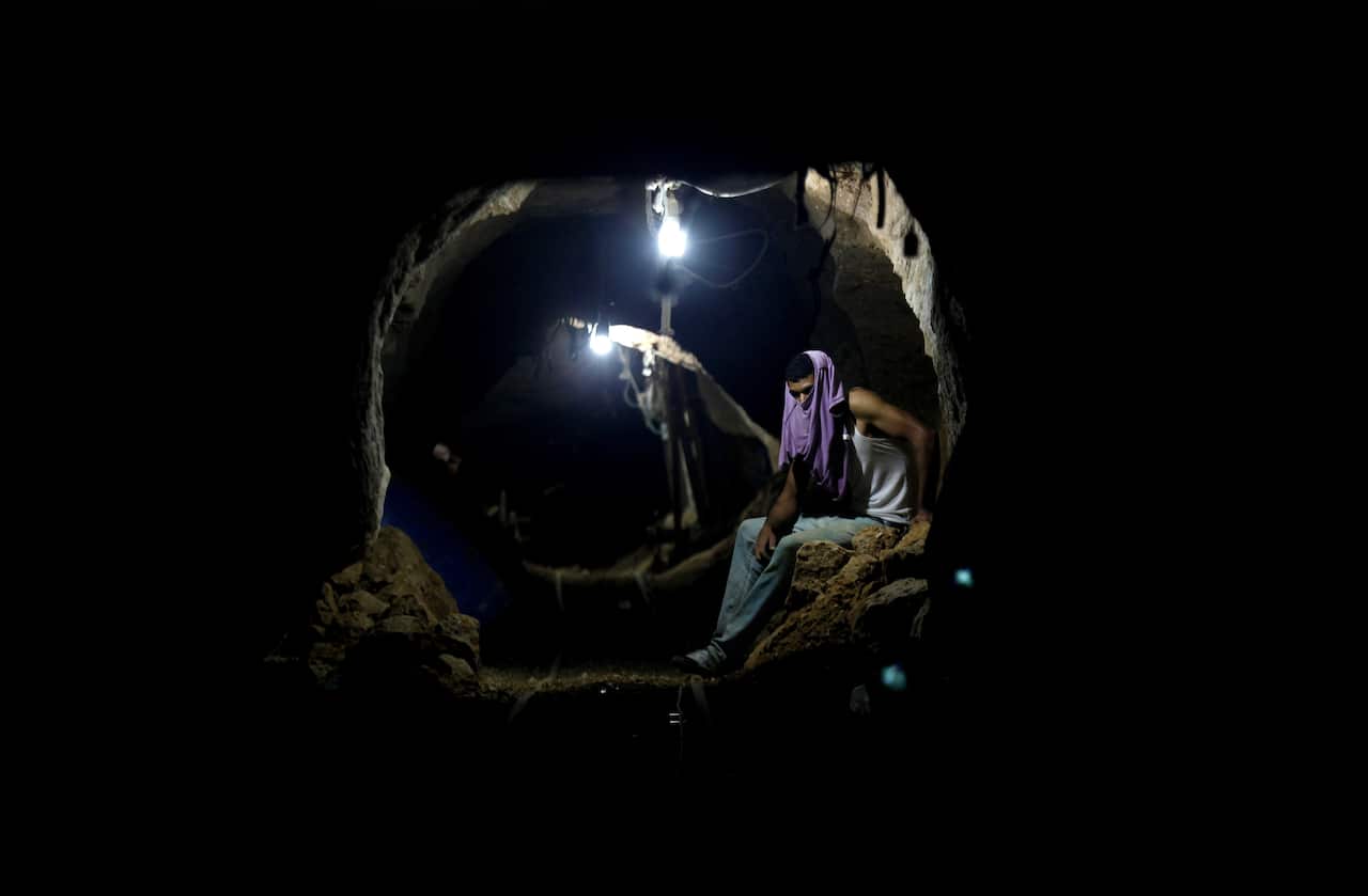 A man with a t-shirt covering his face sits inside a tunnel.