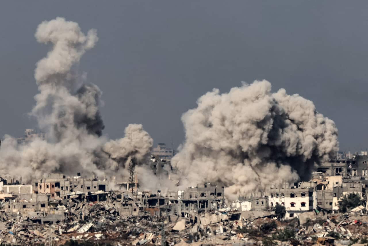 A large plume of smoke rises from a region of Gaza, with rubble and destruction visible in the foreground.