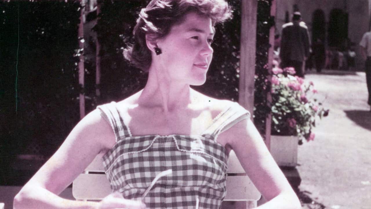 a vintage photograph of a young woman in a chequered dress sitting outside in a cafe with roses in the background