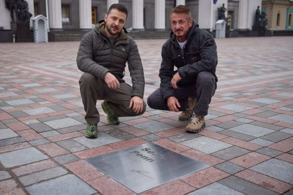Two men squatting at a plaque in paving