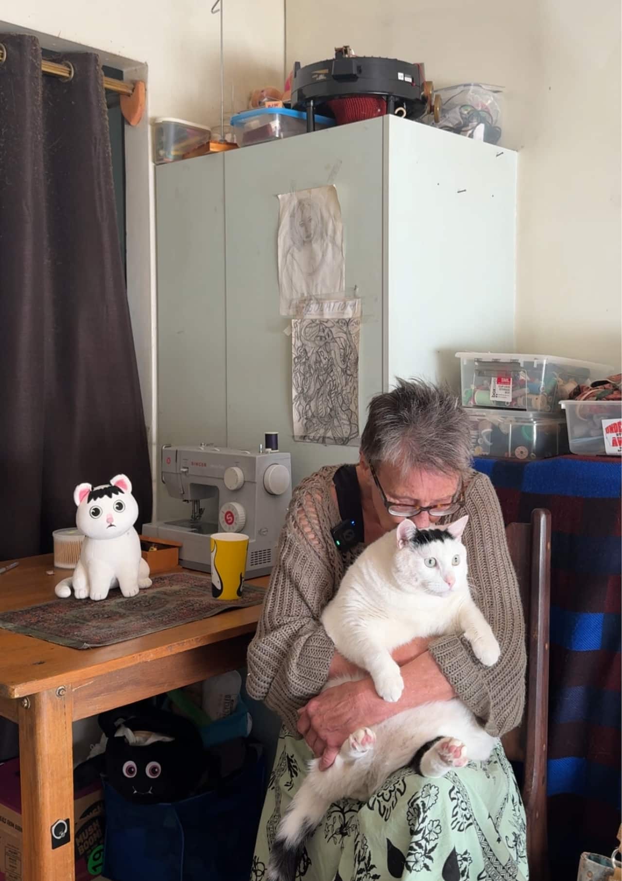 A woman kissing her cat as she sits next to a wooden table.