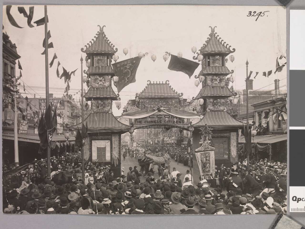 A black and white photo of a crowd gathered around a Chinese pagoda-style arch with a dragon underneath