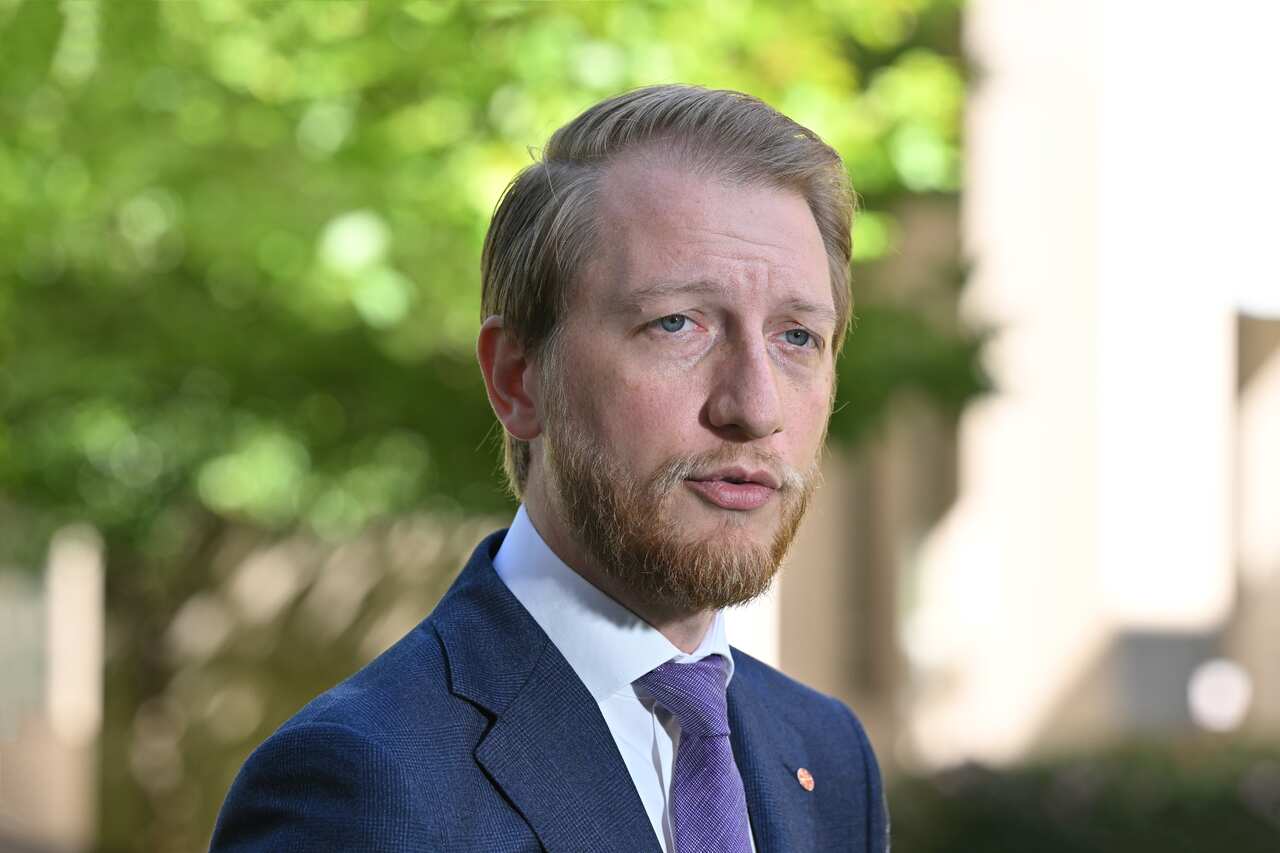Man with beard in a suit talks in a courtyard.