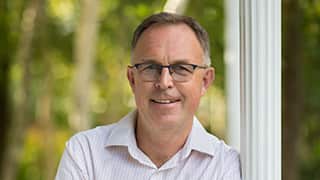 A white man in glasses leans against a pillar