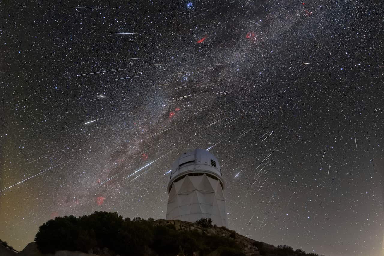 White streaks in night sky above an observatory.