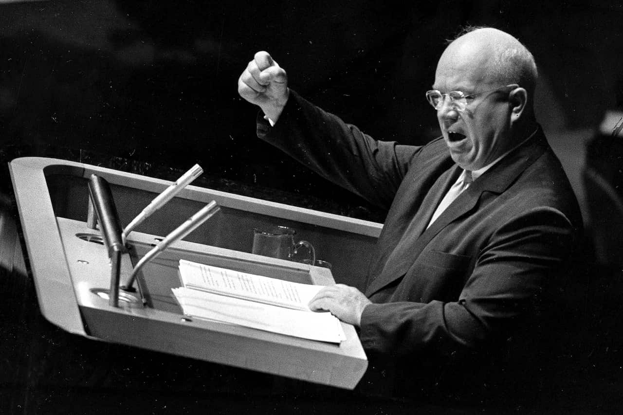 A black-and-white photo of an older man in a suit, speaking at a podium