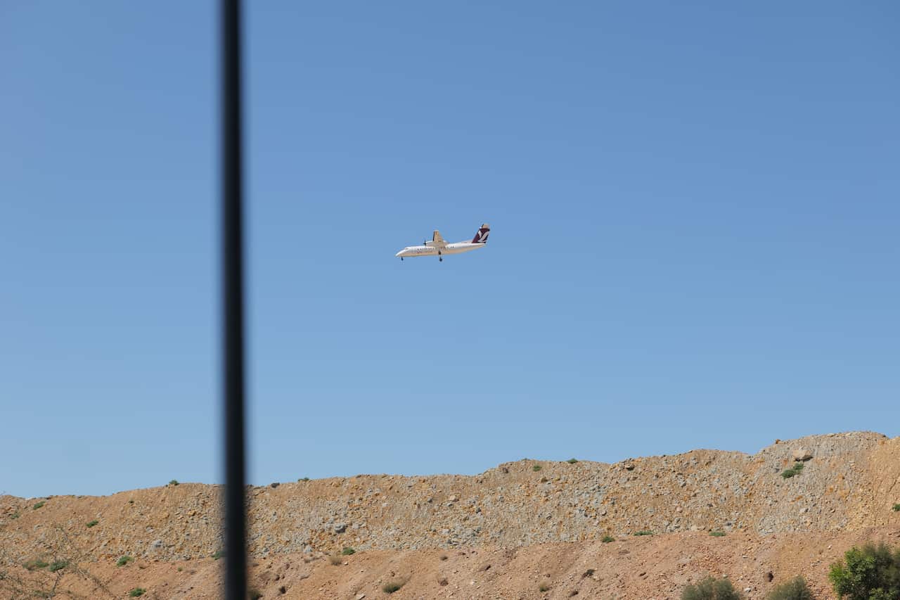 A plane landing over a dirt embankment.
