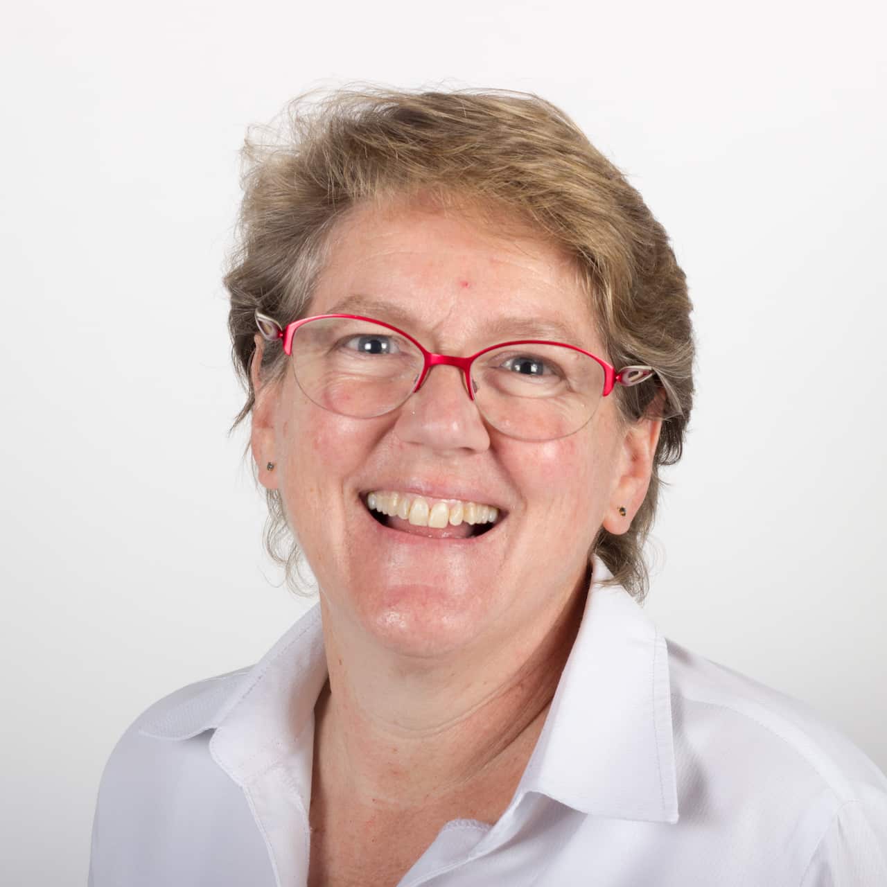 A woman in a white shirt and red rimmed glasses is smiling.