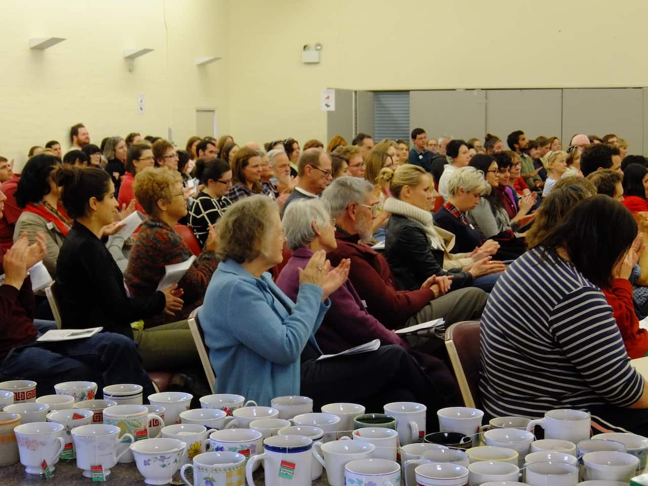 A crowd is pictured at a gathering, with tea cups in the foreground.jpg