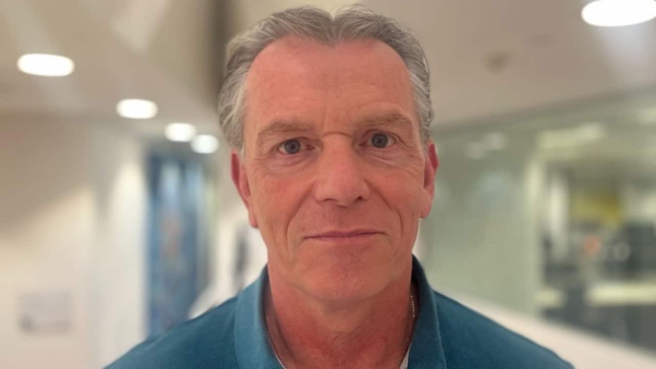 a closeup shot of a middle aged man with grey hair in a blue shirt