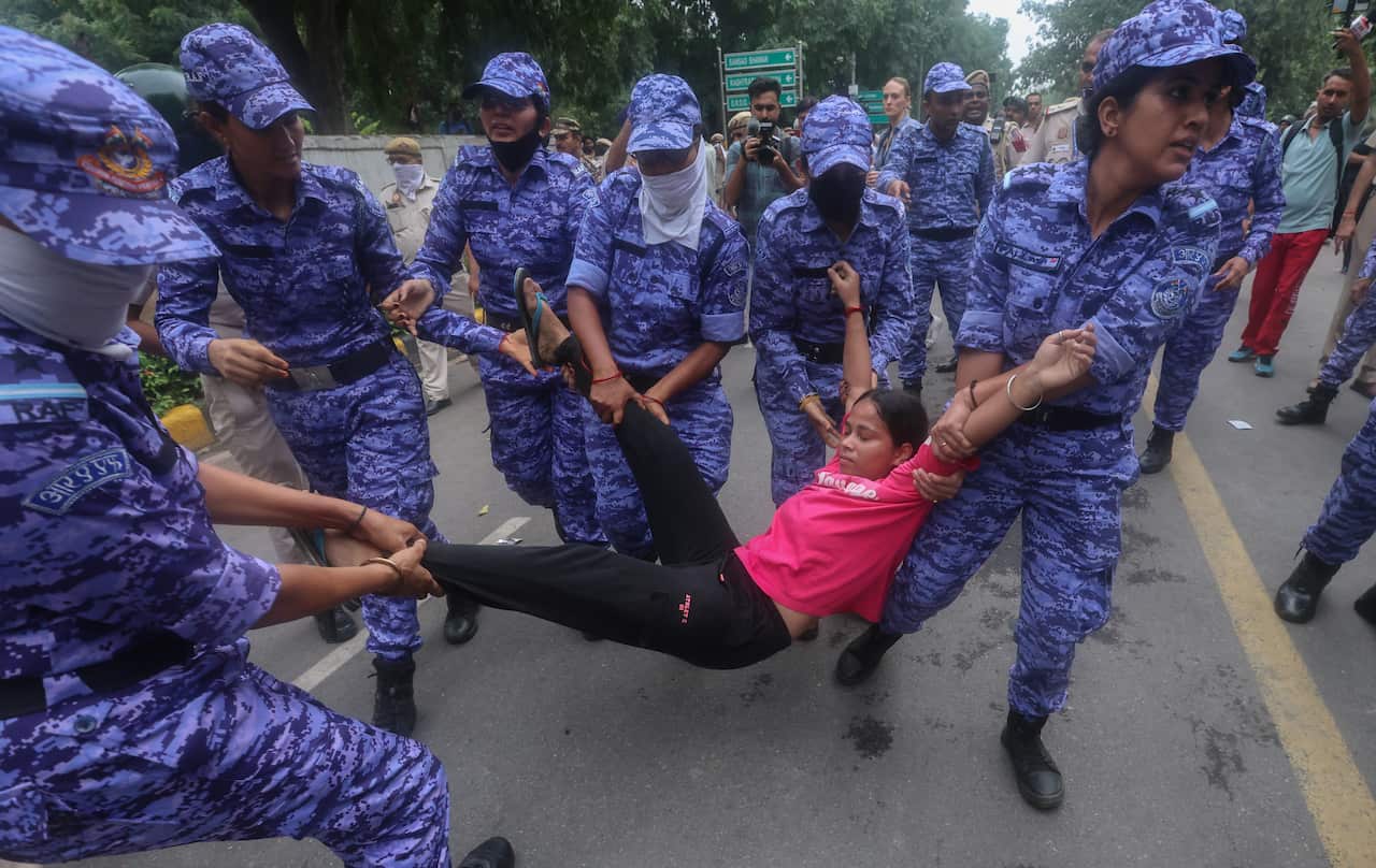 Security personnel lift up a person wearing a pink t-shirt by her legs and hands