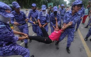 Security personnel lift up a person wearing a pink t-shirt by her legs and hands