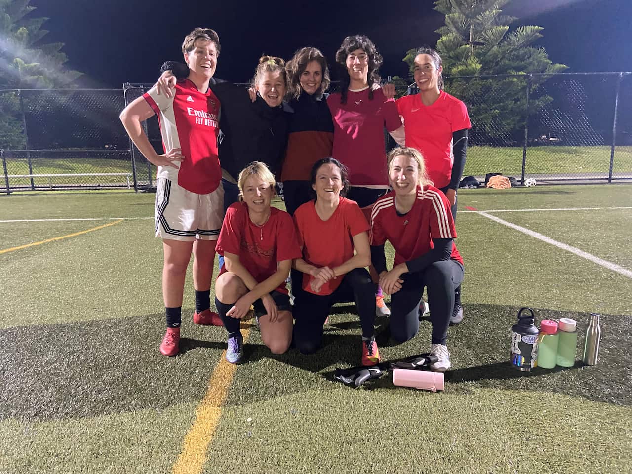 Nine women in red football shirts. Five are standing and four are kneeling in front.