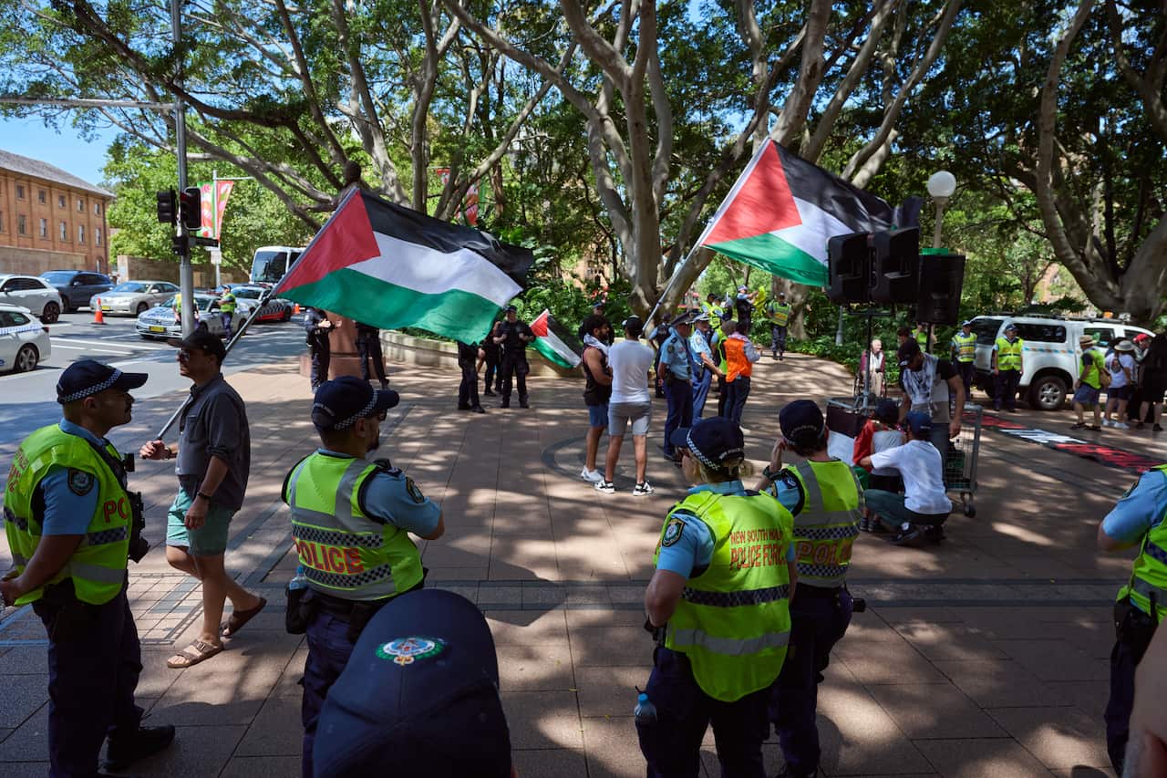 A small group of people holding Palestinian flags outside being watched by police in yellow vests 